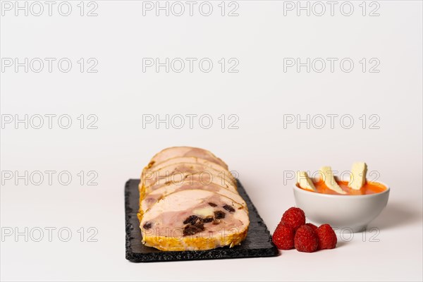 Close-up of a chicken stuffed with raspberry and goat cheese with a bowl of raspberry sauce isolated on white background