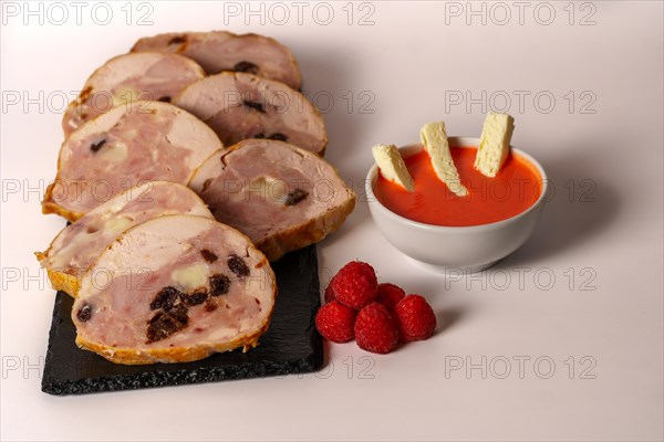 Close-up of a chicken stuffed with raspberry and goat cheese with a bowl of raspberry sauce isolated on white background