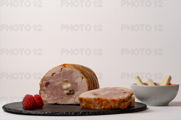 Close-up of a chicken stuffed with raspberry and goat cheese with a bowl of raspberry sauce isolated on white background