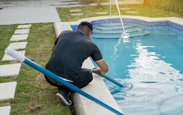 Maintenance person cleaning swimming pool with suction hose