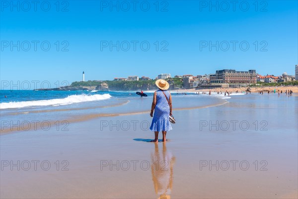 An elderly woman with a hat walking on the beach in Biarritz