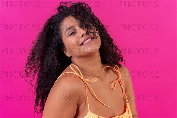 Curly-haired woman in summer clothes on a pink background having fun