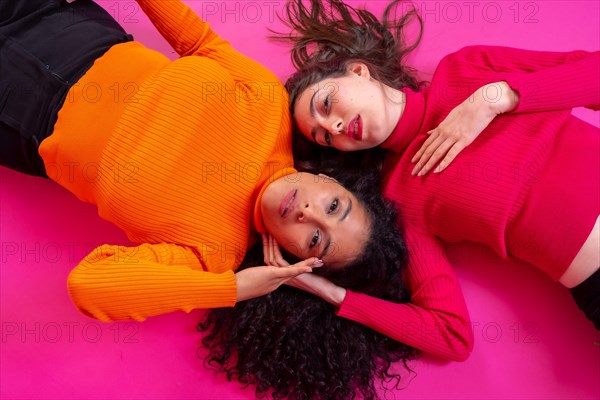 Two multi-ethnic women lying in a trendy posing on a pink background