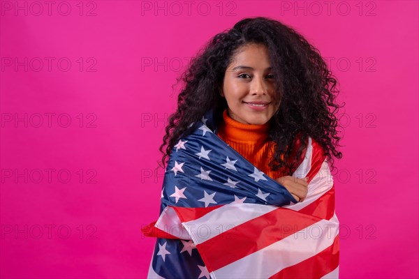 Portrait of a curly-haired woman smiling with the usa flag on a pink background