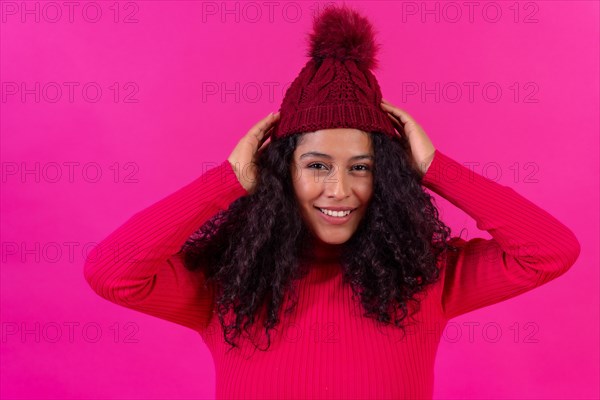 Portrait curly-haired woman in a wool hat on a pink background