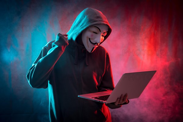 Hacker with an anonymous mask with a computer and making a fight symbol