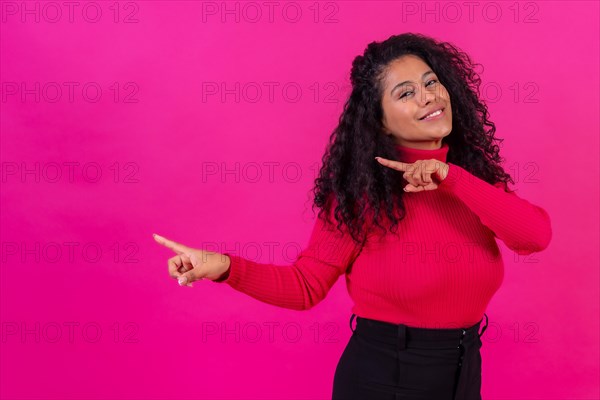 Curly-haired woman pointing left on a pink background