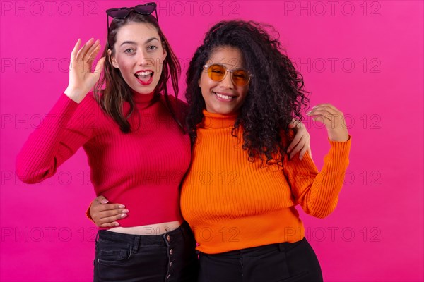 Female friends in sunglasses having fun and smiling on a pink background