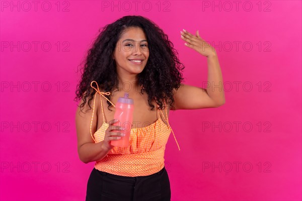Curly-haired woman in summer clothes on a pink background drinking heated water