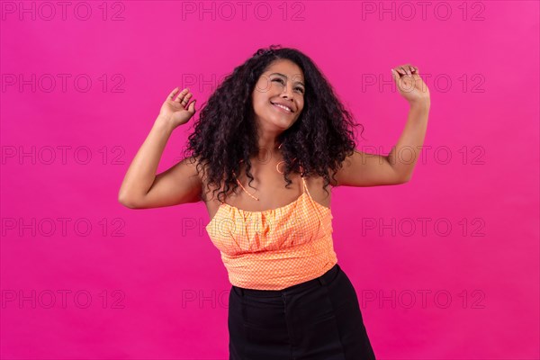 Curly-haired woman in summer clothes on a pink background dancing