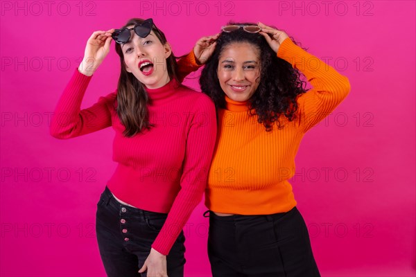 Portrait female friends in sunglasses having fun on a pink background