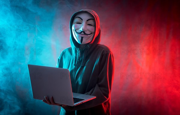 Hacker with anonymous mask with a computer and with a background of smoke and colored led