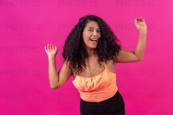 Curly-haired woman in summer clothes on a pink background dancing