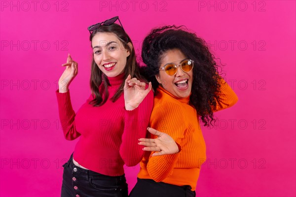 Female friends in sunglasses having fun and dancing on a pink background