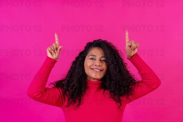 Curly-haired woman pointing up on a pink background
