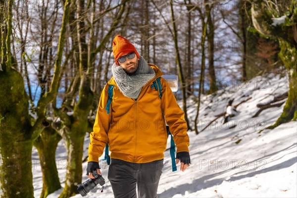 Portrait of a photographer trekking with a backpack taking photos in a beech forest with snow