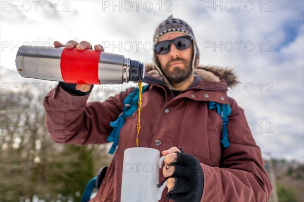 Man having breakfast a hot coffee from a thermos in winter in the snow before starting the trekking