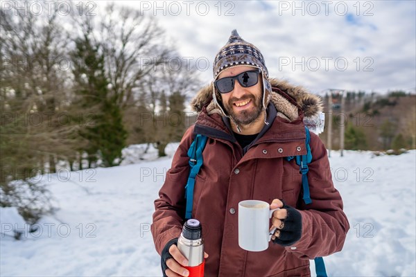 Portrait of man having breakfast a hot coffee from a thermos in winter in the snow
