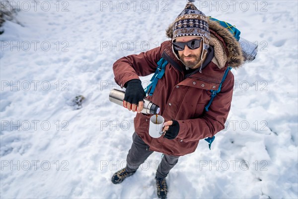 Portrait of man having breakfast a hot coffee from a thermos in winter in the snow before starting the trekking