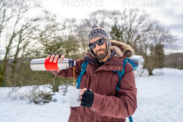 Portrait of man having breakfast a hot coffee from a thermos in winter in the snow before starting the trekking