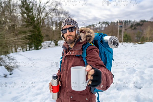 Portrait of man having breakfast a hot coffee from a thermos in winter in the snow