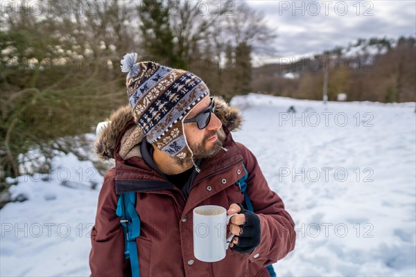 Portrait of man having breakfast a hot coffee from a thermos in winter in the snow before starting the trekking