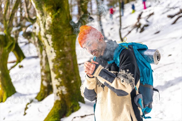 A man smoking lighting a cigarette with a lighter on a snowy mountain in winter