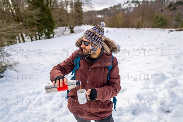 Man drinking coffee from a hot thermos in winter in the snow before starting the trekking