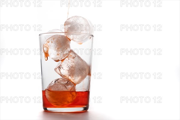 Crystal glass with ices pouring red cocktail on white background and copy space