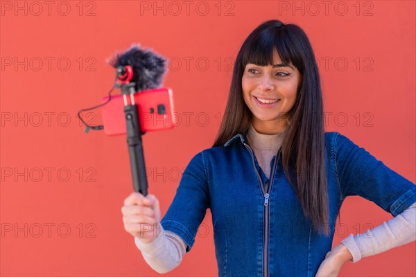 Brunette girl recording a video blog with the mobile phone in a blue denim outfit for social networks