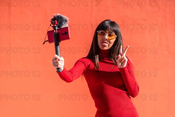 Brunette girl making the victory sign recording a video blog with the mobile