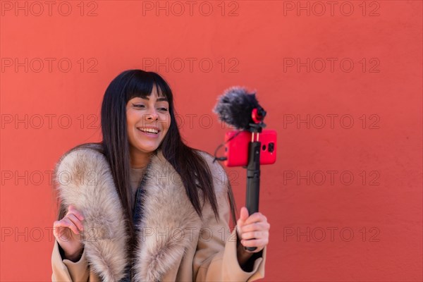 Smiling brunette girl recording a video blog with her mobile phone and microphone