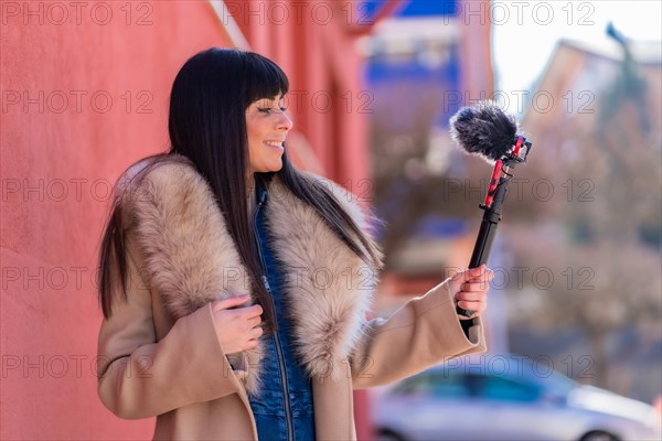 Brunette girl smiling and waving while recording a video blog with her mobile phone and microphone