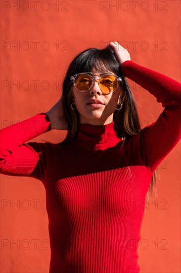 Portrait of a brunette girl with her hands on her faces wearing an orange dress and sunglasses in spring