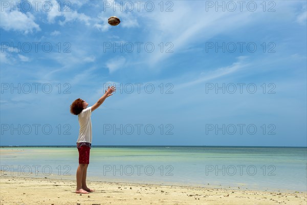 Young man throws a coconut in the air on the beach