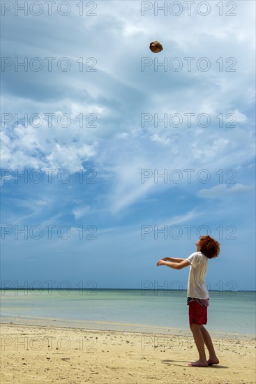 Young man throws a coconut in the air on the beach