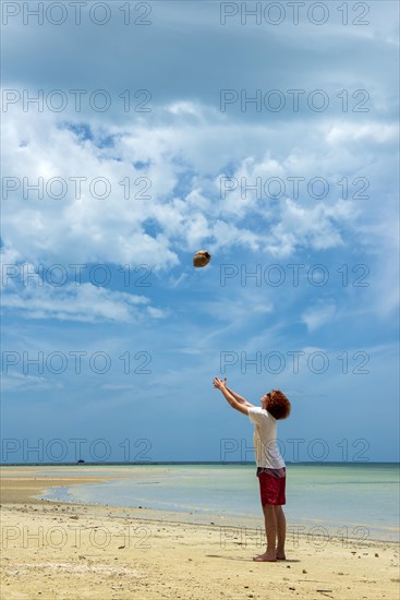 Young man throws a coconut in the air on the beach