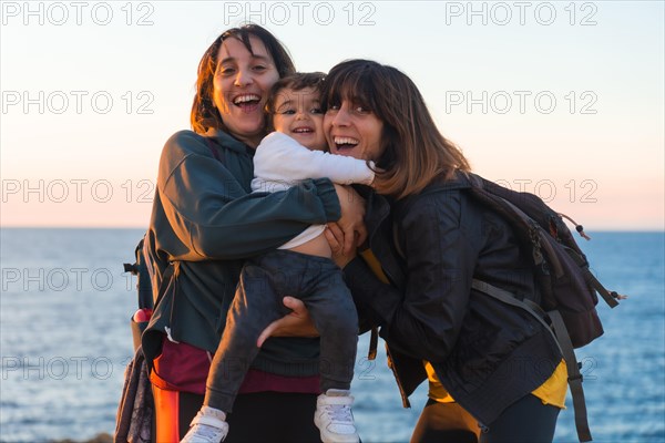 Aunt of the child and mother hugging with him child on the coast by the sea at sunset