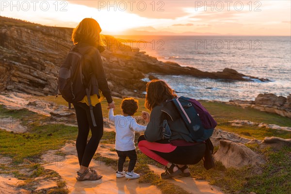 Lgbt couple of women with a child looking at the sunset on the coast by the sea