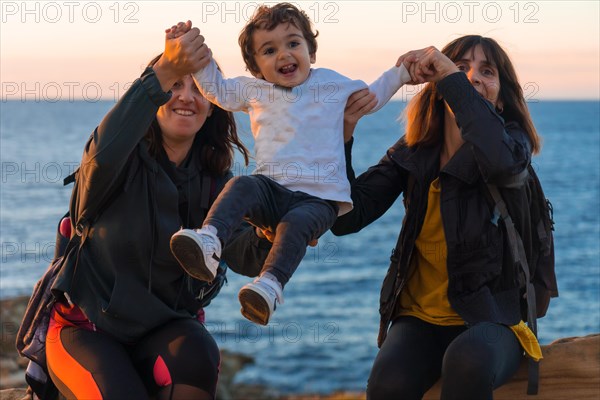 Aunt of the child and mother playing with him child on the coast by the sea at sunset