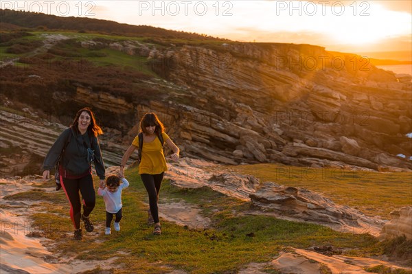 Two sisters with a child watching the sunset on the coast by the sea