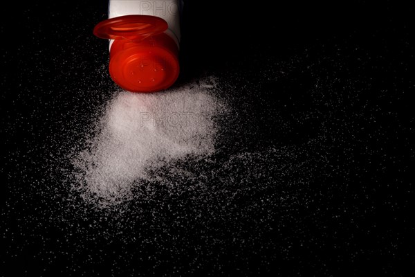 Close-up of a red salt shaker with spilled salt on a black table