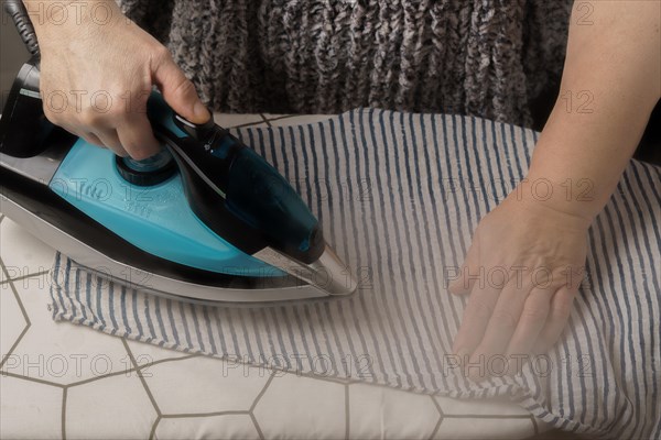 Woman ironing a striped T-shirt by steaming the iron