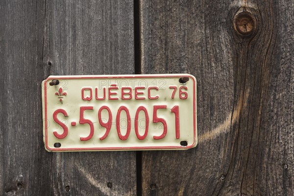 Vintage 1976 Quebec province license plate displayed on side wall of wood plank storage shed