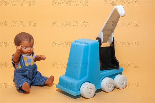 A car crane and a little dolls boy set against a beige background