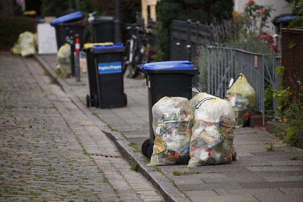 Blue bins for waste paper and yellow bags for plastic waste standing on the street