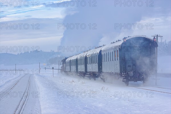 A train pulled by a steam locomotive travels over the snowy winter landscape