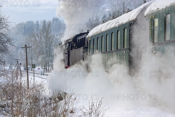 A train pulled by a steam locomotive travels over the snowy winter landscape
