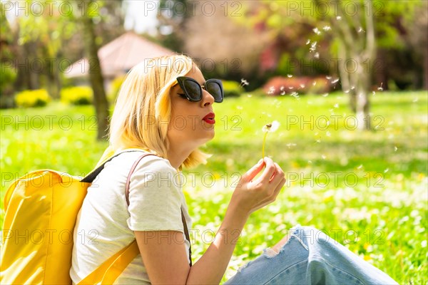 A tourist blonde woman blowing dandelion plant