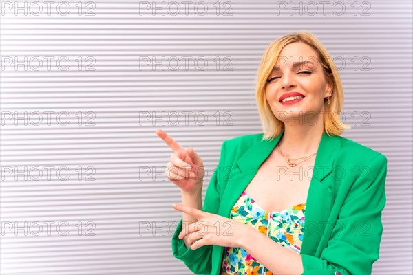 Portrait of a pretty blonde model in a green jacket pointing to the left